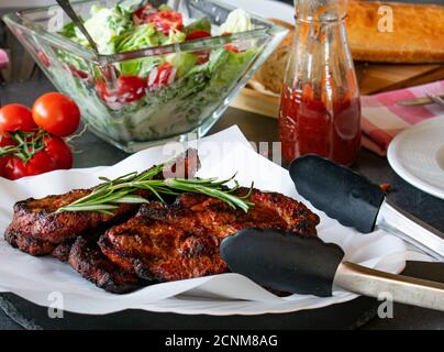 Gegrillte Schweinesteaks mit hausgemachter Barbecue-Sauce serviert mit frischen Salat auf einem Tisch Stockfoto