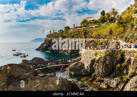 Schöner landschaftlicher Panoramablick auf das Küstengebiet in Manarola in der Nähe des Yachthafens an einem sonnigen Tag mit blauem Himmel. Besucher gehen die Klippe hinauf zum... Stockfoto