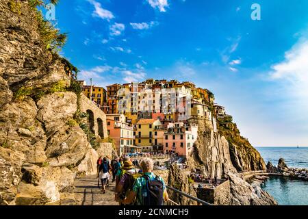 Herrliche Aussicht auf die historischen bunten Häuser in Manarola an der Küste von Cinque Terre an einem sonnigen Tag mit blauem Himmel. Die Menschen auf dem Weg sind... Stockfoto