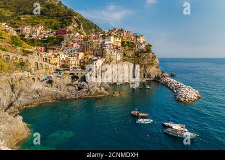 Fantastischer Panoramablick auf die Manarola Marina mit verankerten Booten und die alten bunten Häuser auf der felsigen Klippe mit Weinbergen im Hintergrund... Stockfoto