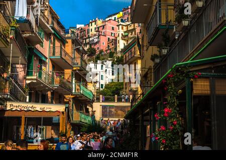 Toller Blick auf die Stadt mitten auf der belebten Straße Via Renato Birolli, voll mit Menschen, die durch die alten bunten Häuser von Manarola, einem der... Stockfoto