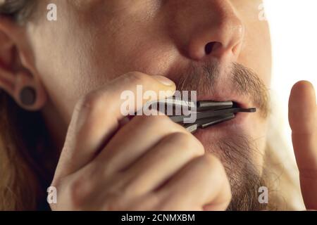 Mann spielt Maultrommel in Aktion isoliert auf weißem Studiohintergrund. Nahaufnahme des Mannes, der ein vibrierendes Instrument zur Meditation spielt. Altes asiatisches Musikinstrument. Konzept der Musik, Hobby. Stockfoto