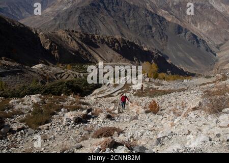 Fotograf und Model wandern an einem klaren Tag zu einem Hügel mit dem sichtbaren Mond, Nako Village, einem See, gelben Bäumen und strukturierten Bergen. Stockfoto