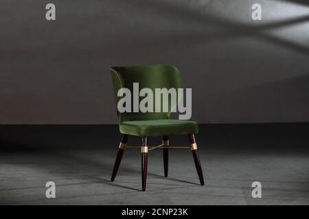 Gemütlicher grüner Ohrensessel in einem Studio mit grauen Wänden Stockfoto