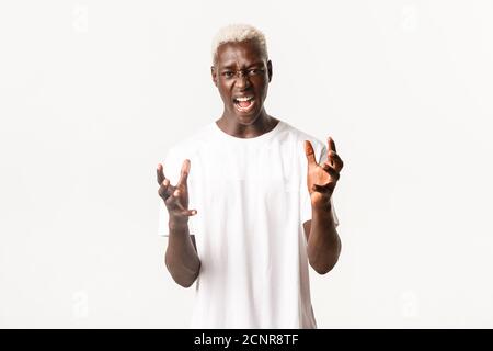 Porträt des verrückten afroamerikanischen blonden Mannes, Hände zusammenklammend und fluchend, schreiend wütend, schauend wütend über weißem Hintergrund Stockfoto