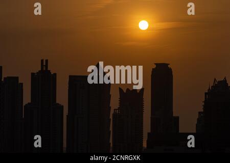 Skyline von Dubai bei Sonnenuntergang mit orangefarbenem und gelbem Himmel über den Wolkenkratzern in den Vereinigten Arabischen Emiraten. Stockfoto