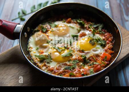 Shakshuka, eine mittelöstliche Delikatesse in einer schwarzen Pfanne auf einer Holzplatte auf einem Hintergrund Stockfoto