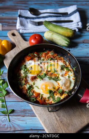Shakshuka, ein tunesisches Gericht in einer schwarzen Pfanne zusammen mit Gewürzen auf einem Hintergrund Stockfoto