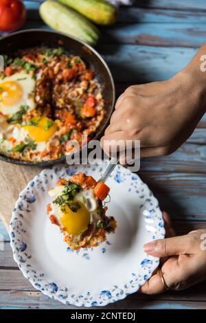 Shakshuka, ein tunesisches Gericht in einer schwarzen Pfanne mit einer Portion auf einem weißen Teller auf einem Hintergrund serviert Stockfoto