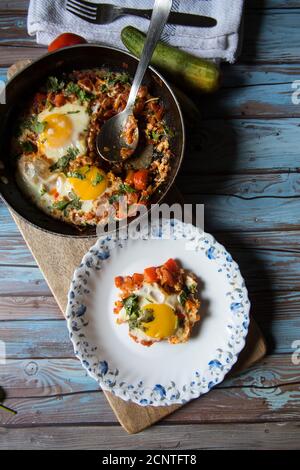 Shakshuka, ein tunesisches Gericht in einer schwarzen Pfanne mit einer Portion auf einem weißen Teller serviert. Stockfoto