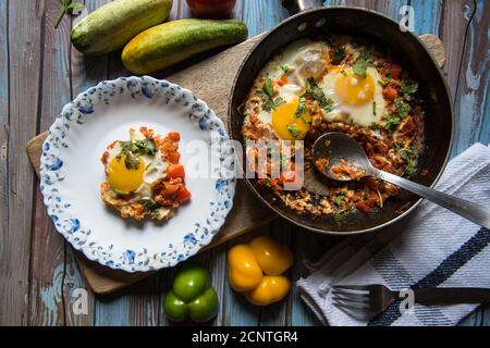 Draufsicht auf Shakshuka, ein tunesisches Gericht in einer schwarzen Pfanne mit einer Portion serviert auf einem weißen Teller auf einem Hintergrund Stockfoto