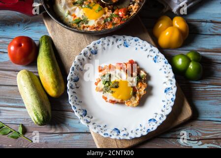 Blick von oben auf Shakshuka, ein tunesisches Gericht in einer schwarzen Pfanne mit einer Portion auf einem weißen Teller auf einem Hintergrund serviert Stockfoto