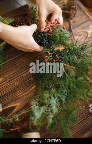 Machen stilvolle rustikale weihnachtskranz. Hände halten Beeren und Dekoration natürlichen Kranz auf rustikalen Holzhintergrund. Saisonurlaub Workshop oder Stockfoto