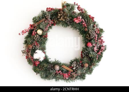 Weihnachtskranz hängt an der weißen Wand im Haus.Traditioneller weihnachtskranz mit roten Beeren und Ornamenten, Pinienzapfen und Zimt isoliert auf weiß Stockfoto