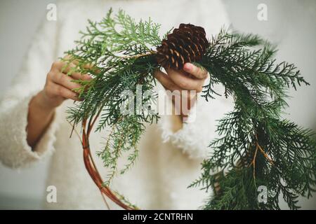 Rustikaler weihnachtskranz in weiblichen Händen. Florist hält modernen natürlichen Kranz mit Kiefer Kegel und Zedernzweige auf weißem Hintergrund. Saisonaler Urlaub Stockfoto