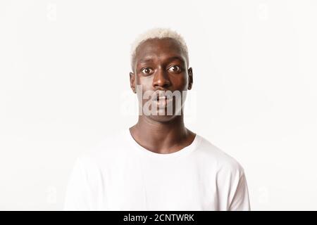 Nahaufnahme von erschrocken keuchenden afroamerikanischen blonden Mann, Drop Kiefer und Blick verwundert an der Kamera, stehend weißen Hintergrund Stockfoto