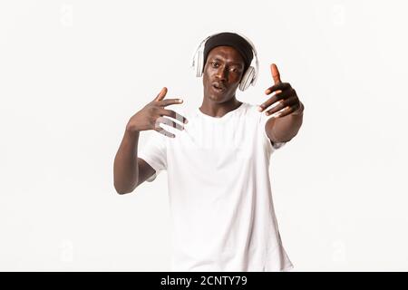 Portrait von fröhlichen kühlen afroamerikanischen Kerl, tanzen und Musik hören in Kopfhörer, weißer Hintergrund Stockfoto