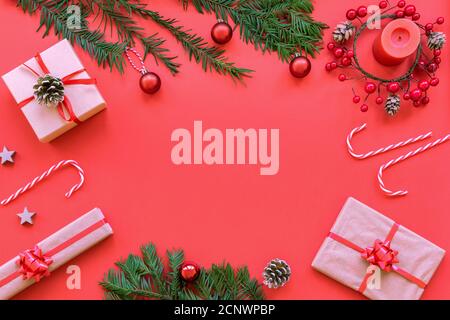 Weihnachts-Layout: Kerze, Kranz, Geschenke in Schachteln, Tannenzweigen, Bonbonstöcke auf rotem Hintergrund, Draufsicht, flach liegend, Kopierraum. Stockfoto