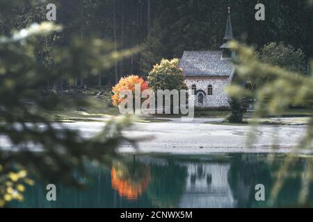 Eine Kirche am Pragser Wildsee, die sich in diesem See widerspiegelt. Neben der Kirche ist ein Baum mit den ersten roten Herbstblättern und es steht Stockfoto