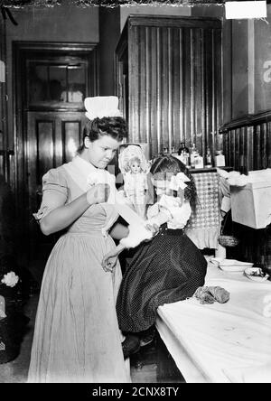 Bild einer Krankenschwester, die den Arm eines Mädchens in einem Raum in Chicago, Illinois, um 1905 verband. Stockfoto