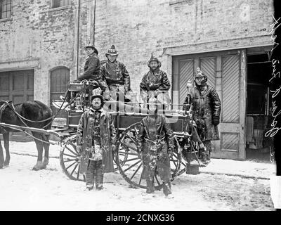 Sechs Mitglieder der Goose Island Fire Department stehen auf und vor einem von Pferden gezogenen Feuerwehrwagen, Chicago, Illinois Stockfoto