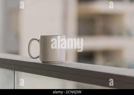 Nahaufnahme der weißen blauen Kaffeetasse auf der Sky-Terrasse am Balkon mit verschwommenem Hintergrund der morgendlichen Stadt. Selektiver Fokus und Kopierbereich. Be Stockfoto