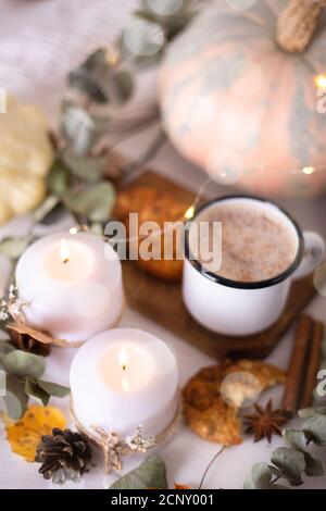 Gemütliche Herbstkomposition. Heißer Kakao mit Keksen in einem weißen Becher mit weißem Strickschal umgeben von Herbstblättern und Kürbissen auf einem weißen Holzbac Stockfoto