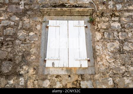 Verwitterte, geschlossene weiße Fensterläden an einem alten verlassenen Steinhaus am Meer. Stockfoto