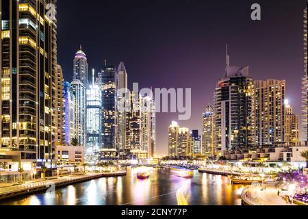 Atemberaubende Aussicht auf den Yachthafen von Dubai mit beleuchteten Wolkenkratzern Der Hintergrund und Licht Wanderwege von einigen Booten verlassen Segeln Im Wasserkanal Stockfoto