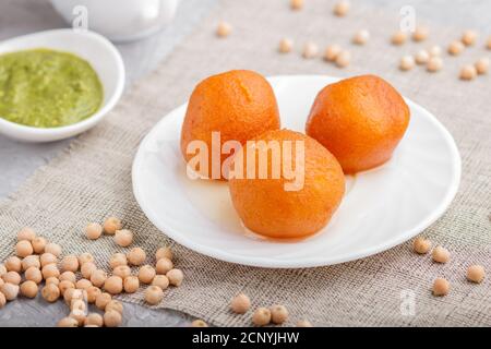 Traditionelle indische Süßigkeiten Gulab Jamun in weißem Teller mit Minze Chutney auf einem grauen Beton Hintergrund. Seitenansicht, close up. Stockfoto