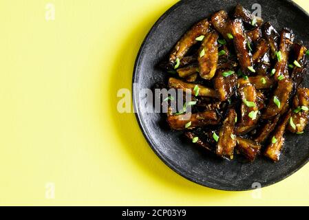 Nahaufnahme der Rührbraten Bulgogi Aubergine auf Platte über gelbem Hintergrund mit freien Text Raum. Gebratene Aubergine im koreanischen Stil. Draufsicht, flach liegend Stockfoto