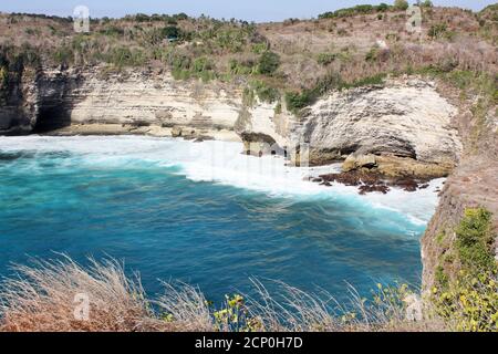 Wellen brechen auf felsigen Ufer am Fuße der steilen Klippen, Nusa Penida, Indonesien Stockfoto