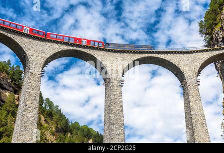 Der Zug fährt auf dem Landwasser Viadukt, Filisur, Schweiz. Dieser Ort ist Wahrzeichen der Schweizer Alpen. Toller Blick auf die hohe Eisenbahnbrücke auf dem Blue Sky Backgro Stockfoto