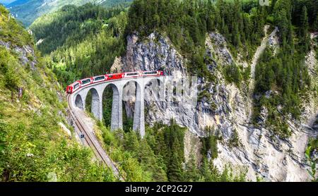 Landschaft mit Landwasserviadukt im Sommer, Filisur, Schweiz. Es ist Wahrzeichen der Schweizer Alpen. Panoramablick auf Eisenbahnbrücke und roten Zug. Rhae Stockfoto