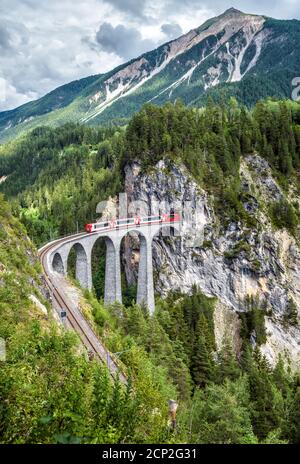 Landwasser Viadukt im Sommer, Filisur, Schweiz. Es ist Wahrzeichen der Schweizer Alpen. Landschaftlich schöner Blick auf die Eisenbahnbrücke und den roten Zug. Alpine Landschaft mit Stockfoto