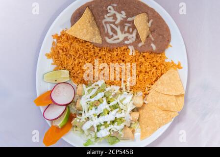 Blick von oben auf Taquitos mit Käse mit Reis und Bohnen auf einer heißen Platte serviert für einige leckere mexikanische Speisen bedeckt. Stockfoto