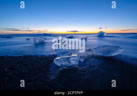 Sonnenaufgang über dem Meer in Island, am Diamond schwarzen Sandstrand mit Licht, das die Eisberge am Strand trifft. Stockfoto