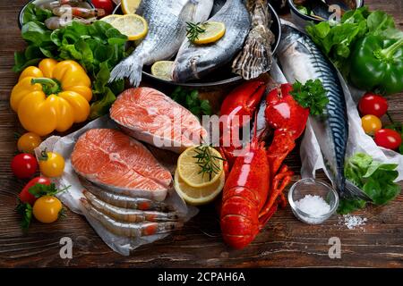 Frischer Fisch und Meeresfrüchte mit Kräutern, Gewürzen und Gemüse auf rustikalem Holzhintergrund. Ausgewogene Ernährung und Kochkonzept. Gesunde Ernährung. Stockfoto