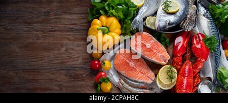 Frischer Fisch und Meeresfrüchte mit Kräutern, Gewürzen und Gemüse auf rustikalem Holzhintergrund. Ausgewogene Ernährung und Kochkonzept. Gesunde Ernährung. Draufsicht mit Stockfoto