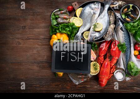 Frischer Fisch und Meeresfrüchte mit Kräutern, Gewürzen und Gemüse auf rustikalem Holzhintergrund. Ausgewogene Ernährung und Kochkonzept. Gesunde Ernährung. Draufsicht mit Stockfoto