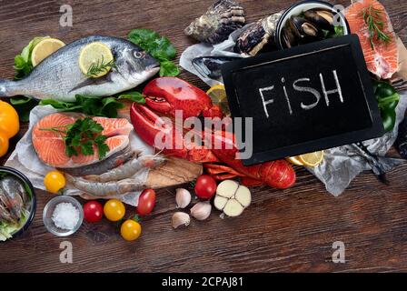 Frischer Fisch und Meeresfrüchte mit Kräutern, Gewürzen und Gemüse auf rustikalem Holzhintergrund. Ausgewogene Ernährung und Kochkonzept. Gesunde Ernährung. Draufsicht Stockfoto