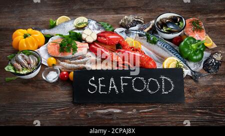 Frischer Fisch und Meeresfrüchte mit Kräutern, Gewürzen und Gemüse auf rustikalem Holzhintergrund. Ausgewogene Ernährung und Kochkonzept. Gesunde Ernährung. Stockfoto