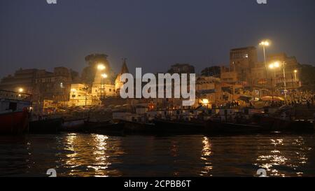 Blick auf Gebäude von Tempeln mit alter Architektur von Varanasi, heilige Hindu-Stadt, wie von einem beweglichen Boot am späten Abend gesehen. Stockfoto