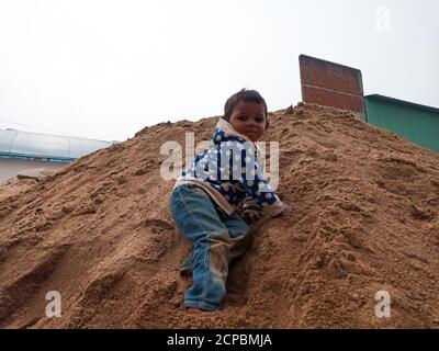 DISTRIKT KATNI, INDIEN - 18. DEZEMBER 2019: Ein indisches Dorf armes männliches Kind, das auf Sandhaufen auf der Baustelle klettert. Stockfoto