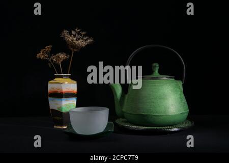 Eine grüne Metallteapot, eine Glasschale und eine chinesische Vase mit getrockneten Dolden. Isoliert auf schwarzem Hintergrund Stockfoto