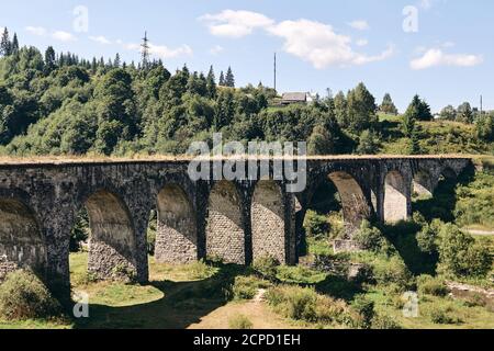 Panoramablick auf die alte Brücke. Viadukt mit alten Bahngleisen in der Nähe von grünen Hügel des Bergwaldes. Lokalisat Reisekonzept Stockfoto