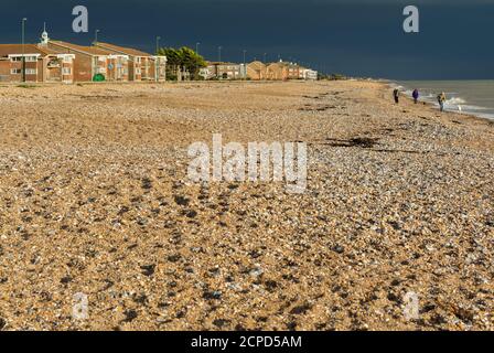 Dunkle Sturmwolken nähern sich der Küste mit Sonnenlicht beleuchtet den Kiesstrand, der fast verlassen, in England, Großbritannien. Stockfoto