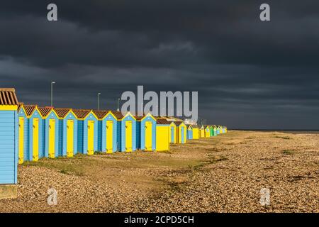 Dunkle Gewitterwolken nähert sich der Küste bei Tageslicht mit der Sonne, Strand Hütten am Strand, in Littlehampton, West Sussex, England, UK. Stockfoto