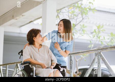 Lächelnder Physiotherapeut, der sich um den glücklichen älteren Patienten kümmert Einen Rollstuhl Stockfoto