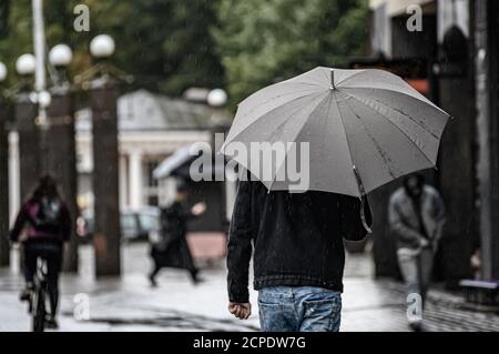 Ein Mann geht die Straße hinunter unter einem grauen Schirm. Regen im Frühherbst. Stockfoto